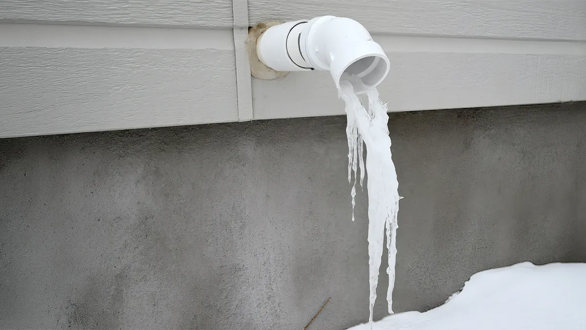 Sump pump discharge pipe coming out of a house foundation with snow piled around it